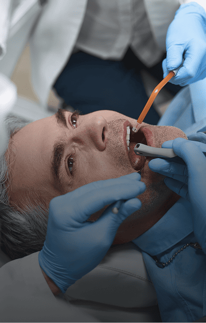 Homem, com a boca aberta, recebendo tratamento odontológico por 2 dentistas